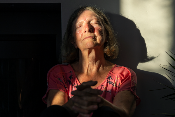 Una mujer mayor satisfecha se sienta contra la pared con los últimos rayos de sol del día calentándole la cara, mientras se toma su tiempo para sentir sus emociones.