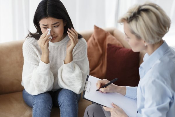 Asian Woman Crying Talking With Psychologist Sitting In Office